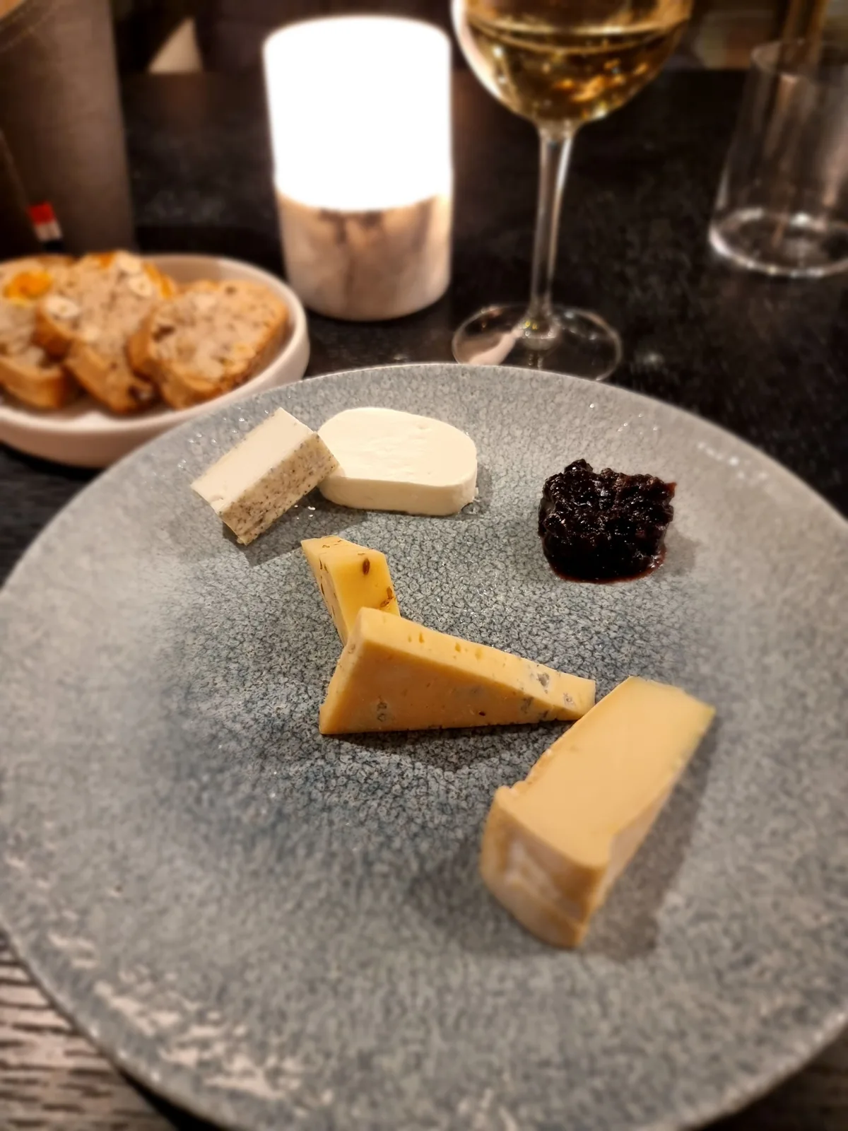 Cheese and preserves on a ceramic plate with bread and a glass of wine