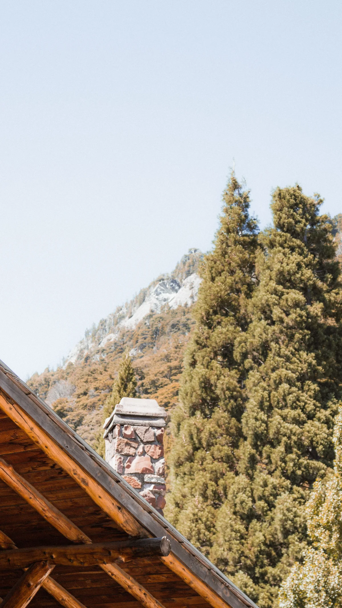 The edge of a timber roof against a wooded mountainside and open sky